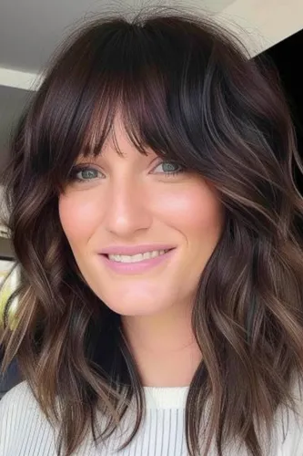 Try on this elegant wavy, ombre hairstyle that transitions from dark roots to lighter tips, emphasizing voluminous, flowing waves.