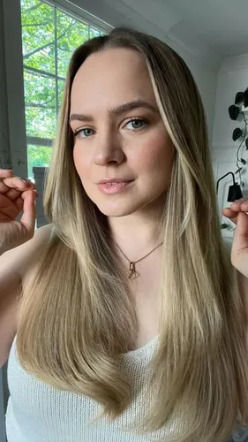 Try on a hairstyle featuring long, straight hair with a natural tone, showcased in an indoor setting with a hint of greenery visible in the background.