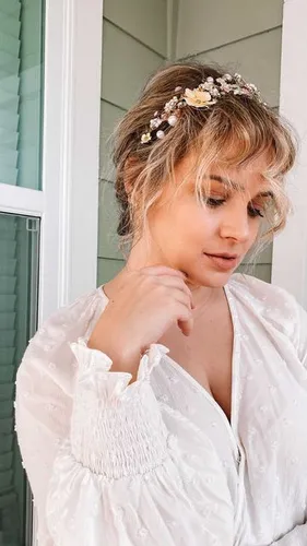 Try on a sophisticated updo hairstyle adorned with a delicate floral headpiece, featuring small white flowers and hints of green leaves, creating a romantic and ethereal look.