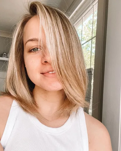 Try on this half-up-half-down hairstyle with strands loosely curling at the bottom, adding a relaxed vibe. The hairstyle features medium-length blonde hair pulled up from the face partially while the rest cascades softly on the shoulders.