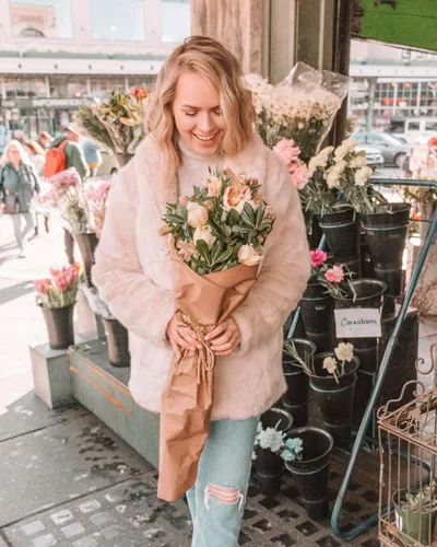 Try on a medium length hairstyle. The person is portrayed in an outdoor setting, holding a bouquet of flowers, suggesting a casual, stylish appearance with a medium length hairstyle.