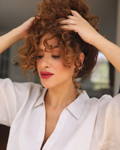 Try on this voluminous curly hairstyle, showcased by a woman adjusting her thick, curly locks.