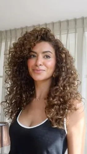 Try on this voluminous long curly hairstyle that frames the face beautifully, showcasing well-defined, bouncy curls.