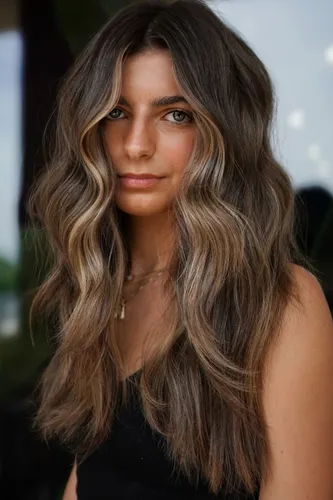 Try on this stylish wavy, ombre hairstyle featuring dark brown roots that gracefully transition into lighter brown and blonde highlights towards the tips, giving a sun-kissed look.