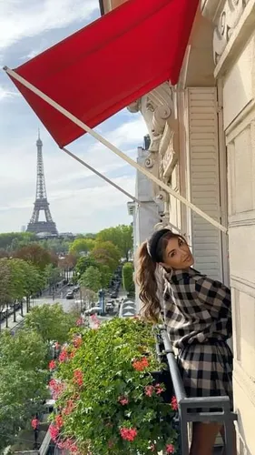 Try on this long, wavy hairstyle as seen on the woman posing on a balcony with a scenic city view in the background.
