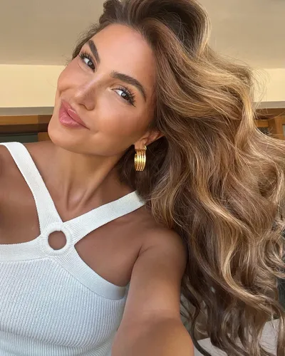 Try on this long wavy hairstyle featuring voluminous, flowy curls in a soft brown tone that gently taper down the shoulders; perfectly showcases a radiant look with a chic, fresh appearance.