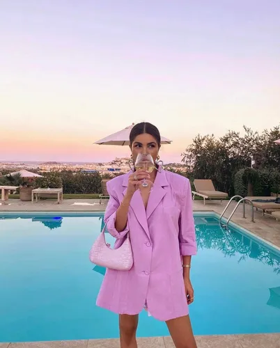 Try on this hairstyle: a woman with a center-parted, straight hairstyle standing by a pool, holding a glass.