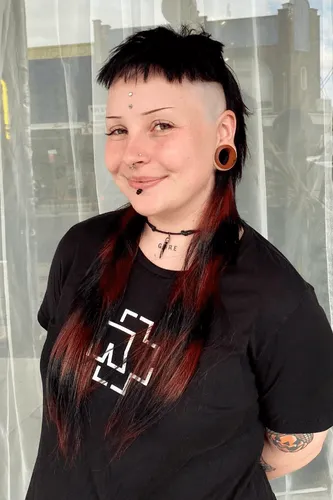 Try on a bold hairstyle featuring shaved sides, a long, sweeping fringe, an undercut, and two-tone hair color emphasizing red highlights contrasting with natural dark tones