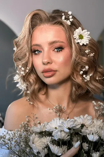 Try on a romantic wavy hairstyle embellished with small white flowers and a prominent white daisy, invoking a whimsical, bridal feel.