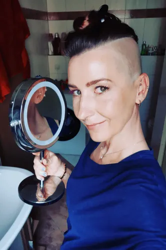 Try on a unique hairstyle featuring a shaved side and a curly top knot. The hairstyle showcases a dramatic contrast with smooth shaved areas and a voluminous curled top, giving a bold and modern look.