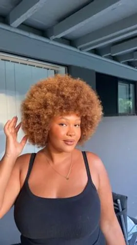Try on this voluminous afro hairstyle that frames the face beautifully with its rounded, dense curls in a natural auburn shade.