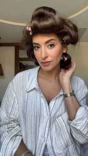 Try on a vintage-inspired hairstyle with voluminous curls and a large swept-up section at the front, complemented by smaller curls secured with hair clips around the head.