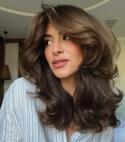 Try on this hairstyle featuring voluminous curls with light brown tones gracefully falling over the shoulders. The hair is parted on the side, adding a soft, frame to the face with ample volume that enhances the stylish and elegant appearance.