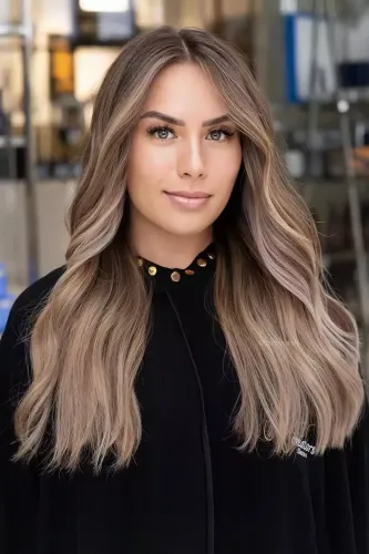 Try on this hairstyle featuring long wavy hair with subtle balayage highlights transitioning from darker roots to lighter ends.