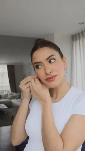 Try on a sleek updo hairstyle, featured by a woman posing with her hand touching her earring, adding a refined touch