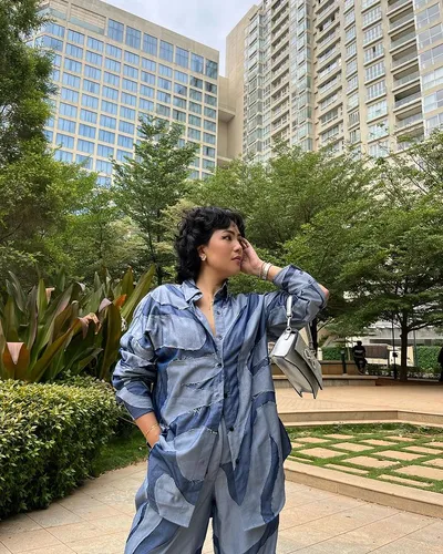 Try on a short, curly hairstyle sported by a person in a denim outfit, standing outdoors.