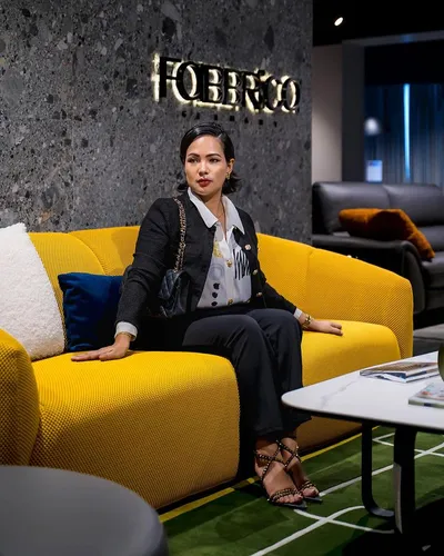 Try on a slicked back hairstyle portrayed by a woman sitting on a yellow couch, facing forward with a confident expression.