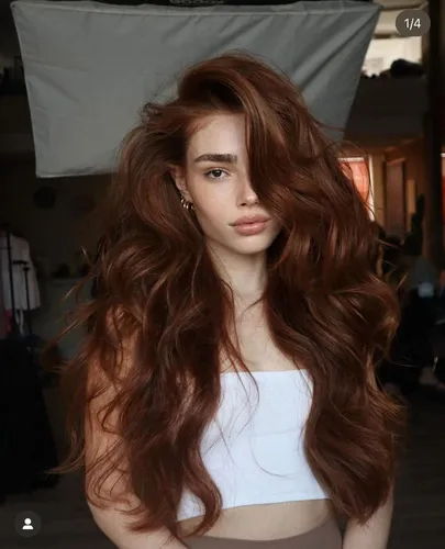 Try on this flowing long wavy hairstyle in red color, featuring luscious curls that add volume and elegance, mainly focusing on the hairstyle with a well-lit indoor background.