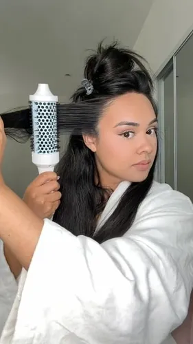 Try on the hairstyle featuring a partial updo with the top section twisted and clipped atop the head while the lower hair flows straight and held by a round brush; a look of styling in progress.