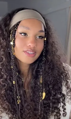 Try on this intricate hairstyle featuring a combination of braids adorned with gold beads and charms, alongside naturally curly textures. The style is complemented by a subtle headband, enhancing the hairstyle's bohemian allure.