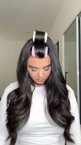Try on a hairstyle featuring long, wavy hair styled with pink and white hair rollers on top. The hair cascades beautifully around the shoulders, showcasing volume and waves.