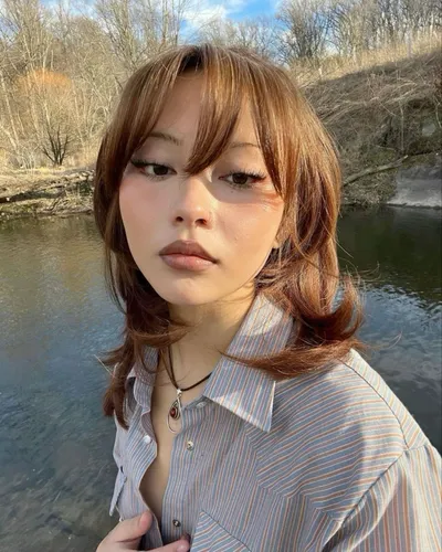 Try on a hairstyle featuring light brown, wavy hair with bangs, giving a soft and natural look.