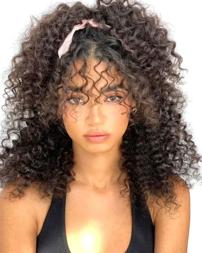 Try on this voluminous curly hairstyle featured in the image, complemented with a light pink headband adding a subtle stylish touch.