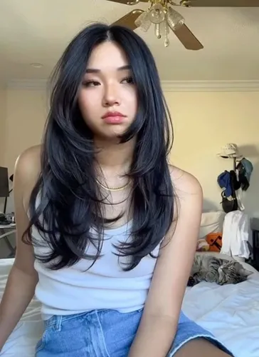 Try on this long, wavy hairstyle featured in the image, with black hair cascading over the shoulders and distinguished by its subtle waves and layers, adding volume and style.