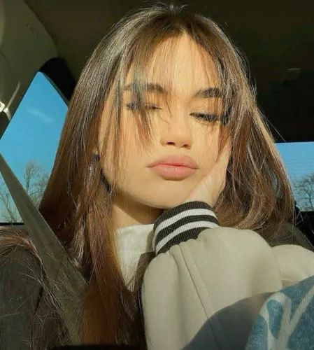 Try on a hairstyle with long hair and soft bangs, highlighted by sunlight, creating a fashion-forward and relaxed look.