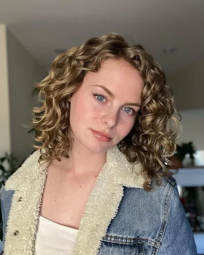 Try on this medium-length curly hairstyle that showcases voluminous curls with defined spirals, adding a touch of bounce and texture.