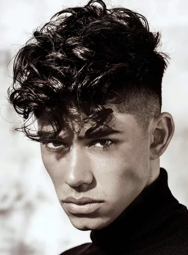 Try on this curly and textured hairstyle with a stylish, voluminous top and closely trimmed sides, showcased by a young man facing forward.