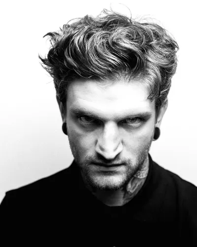 Try on this messy, wavy hairstyle featured on a man facing forward with intense expression.