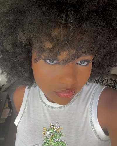 Try on this voluminous afro hairstyle, featuring tightly coiled natural curls that add a lively bounce around the face.