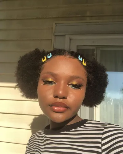 Try on this hairstyle featuring a young woman with natural short hair styled into two puffs, accented with colorful hair accessories