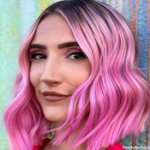 Try on a wavy pink hairstyle with highlighted strands varying in shades of bright pink and pale pink, elegantly styled to showcase a vibrant and youthful look.