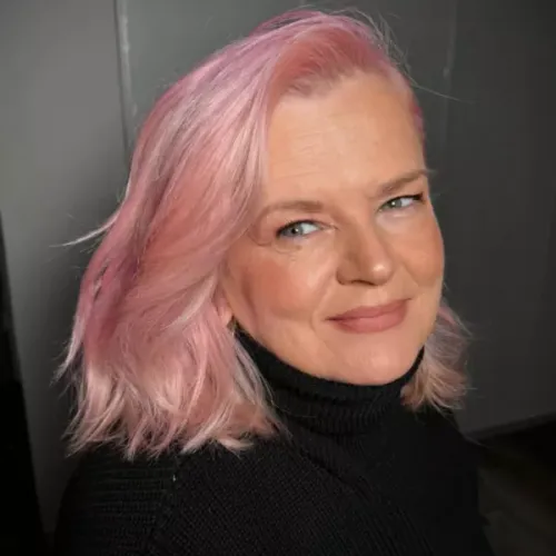 Try on this medium-length, wavy, pink hairstyle showcased by a woman with a gentle smile.