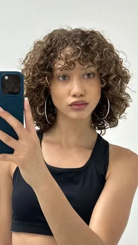 Try on this medium-length curly hairstyle, which features voluminous curls that cascade around the face, presenting a playful and dynamic look.