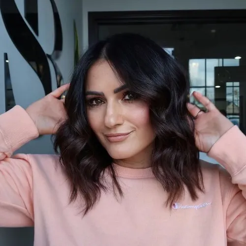 Try on this trendy medium-length wavy hairstyle. The person is smiling directly at the camera, showcasing her stylish brown waves perfectly shaped around her face.