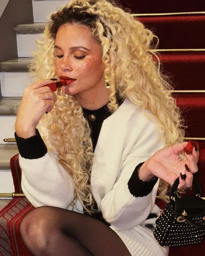 Try on long, voluminous curly blonde hair draped over the shoulders, paired with a white sweater, enhancing the relaxed yet stylish look.