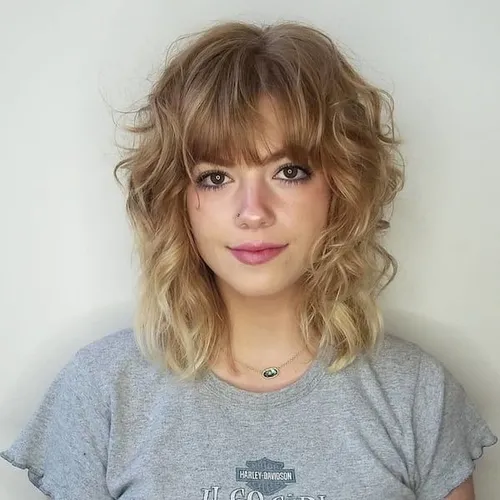 Try this shaggy, curly hairstyle with bangs for a trendy, youthful look, featuring voluminous layers that enhance the bounce and texture of the curls.