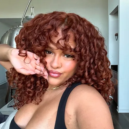 Try on this voluminous auburn curly hairstyle that frames the face with soft, bouncy curls, adding a playful and elegant touch.