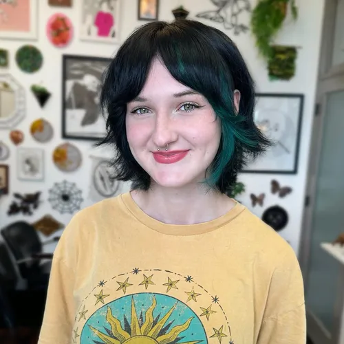Try on this chic hairstyle featuring short black hair with striking green tips, styled in a loose, tousled manner. The hairstyle shows off vibrant personalities and adds a touch of bold color to a casual look.