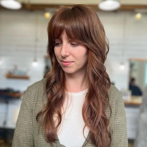 Try on a wavy hairstyle with bangs, featuring chestnut brown color and soft, flowing curls that frame the face gracefully.