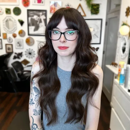 Try on this hairstyle featuring long wavy hair with full bangs, perfectly complementing glasses for a stylish look.
