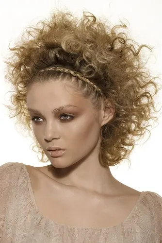 Try on this voluminous curly hairstyle, complemented by a braided headband intertwining through the locks.