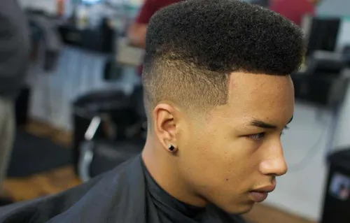 Try on this high-top fade hairstyle, which features neatly clipped sides flowing into a voluminous, textured top. The transition between the lengths creates a distinctive profile that accentuates the shape of the haircut.