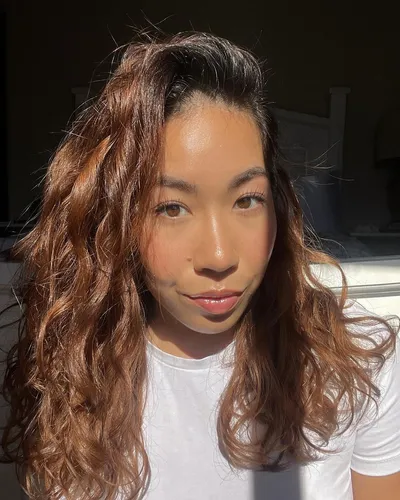 Try on this long wavy hairstyle showcased by a woman, cascading down and illuminated under bright natural light.