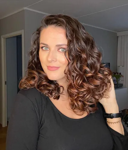 Try on this medium-length curly hairstyle with ombre coloring that transitions from dark brown at the roots to lighter shades at the ends.