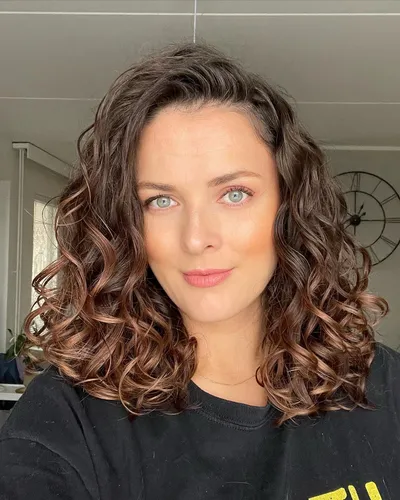 Try on this look featuring shoulder-length brown curly hair styled in loose, bouncy curls, presenting a voluminous and well-defined texture.