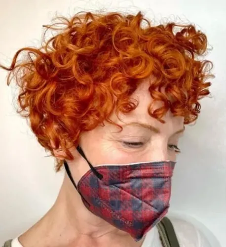 Try on this vibrant reddish-orange, short curly hairstyle